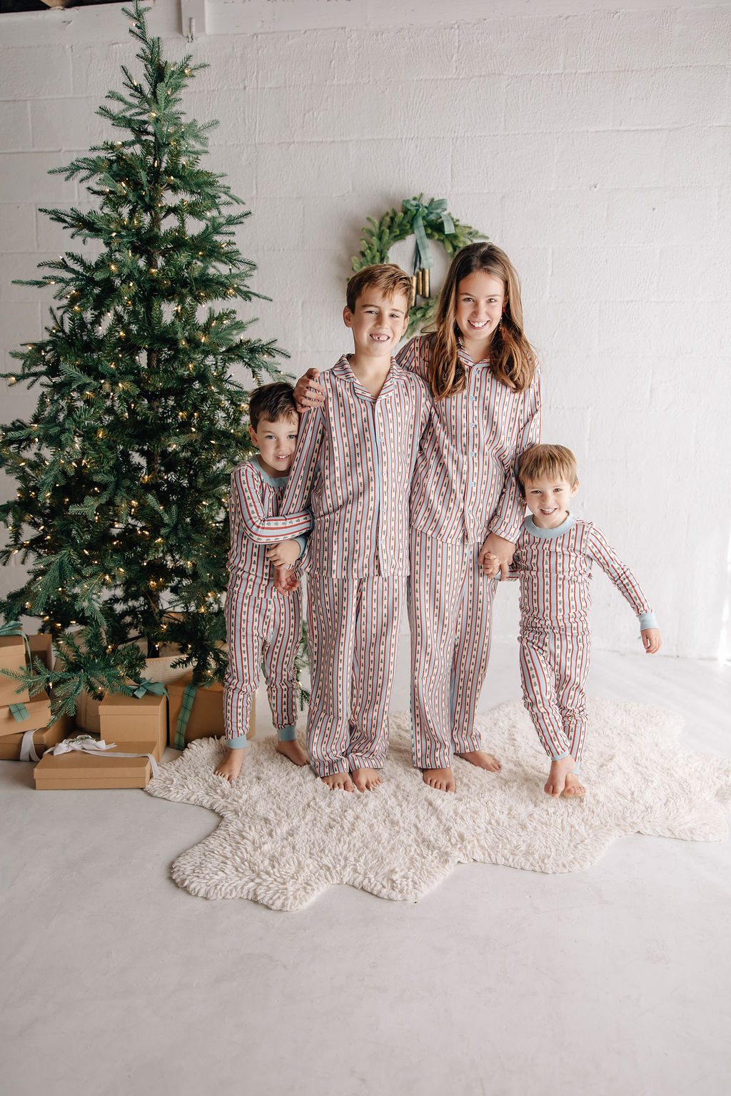 Four siblings in matching pajamas standing in front of a Christmas tree