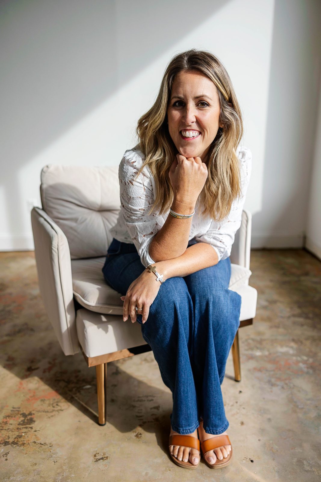 A smiling woman in a cream armchair by a sunlit window