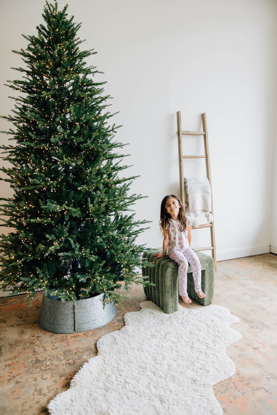 A girl sitting on the green stool next to the Christmas tree in the studio